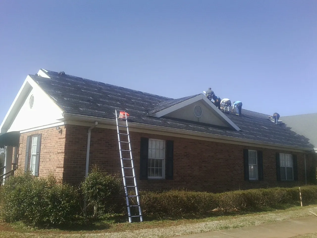 Crew tearing shingles off a brick ranch roof with a ladder set — Emergency Roof Repair work by our crew in Fayetteville