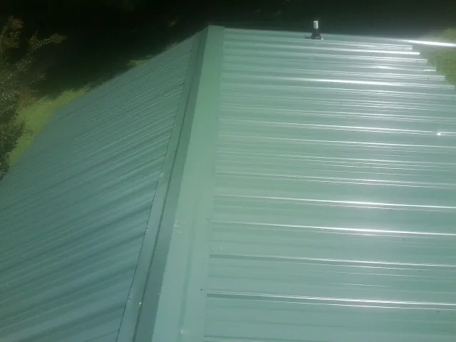 New green metal panels meeting at the ridge of a roof — Flat Roof Repair work by our crew in Fayetteville