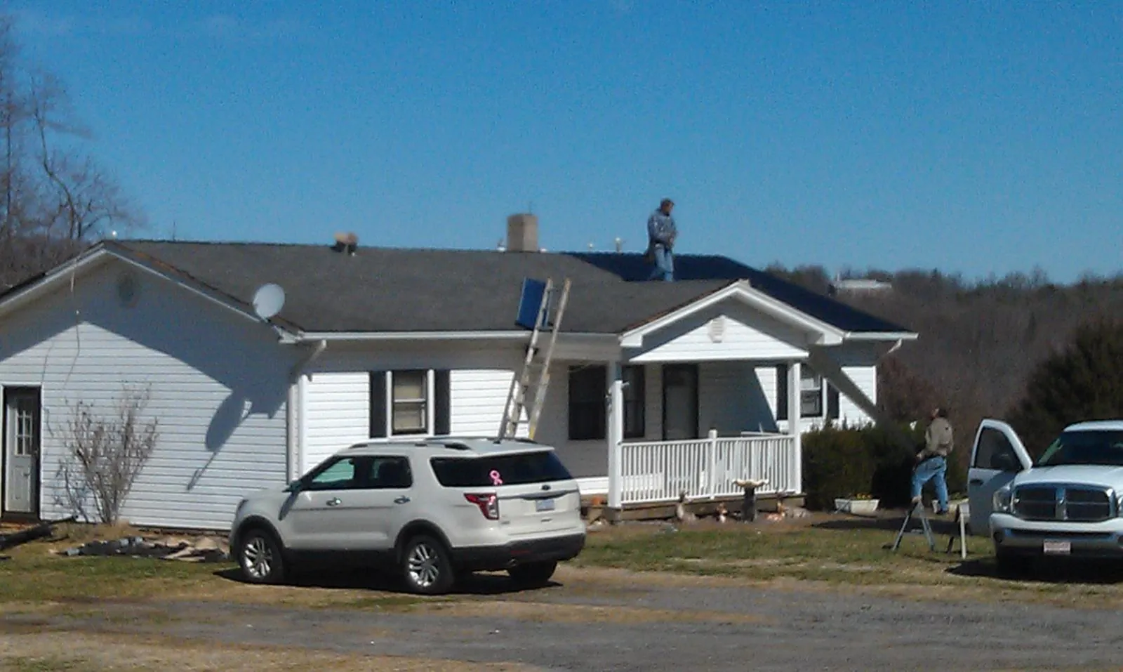 Roofers stripping shingles from a white ranch house roof in Fayetteville